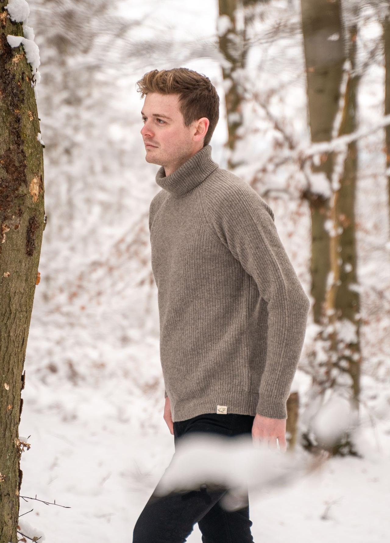 Ein Mann trägt einen grauen Rollkragenpullover und läuft durch Schnee im Wald