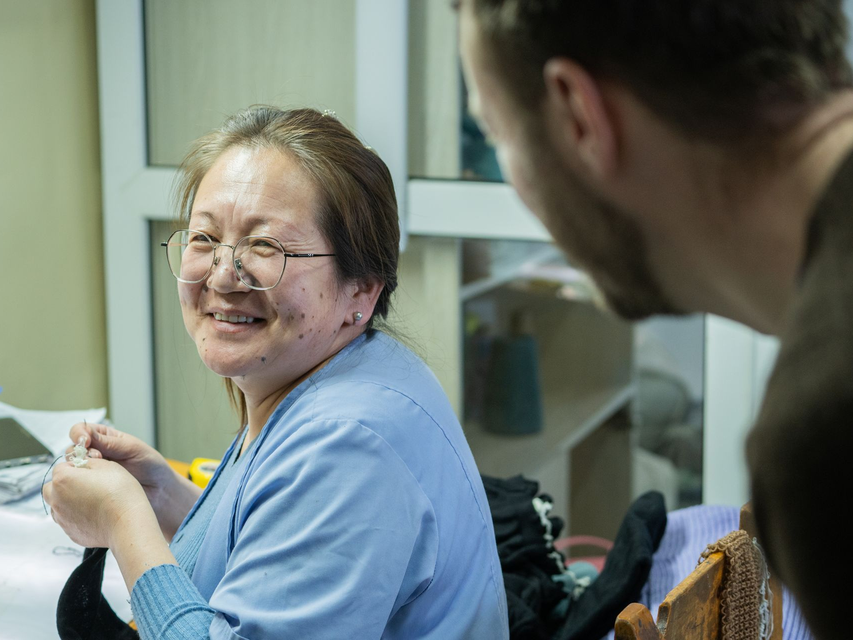 Eine Frau lacht in die Kamera und arbeitet an einem Kleidungsstück in der Mongolei