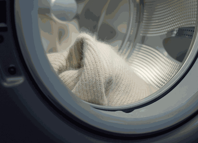 Ein weißes Kleidungsstück aus Wolle liegt in der Waschtrommel einer Waschmaschine.