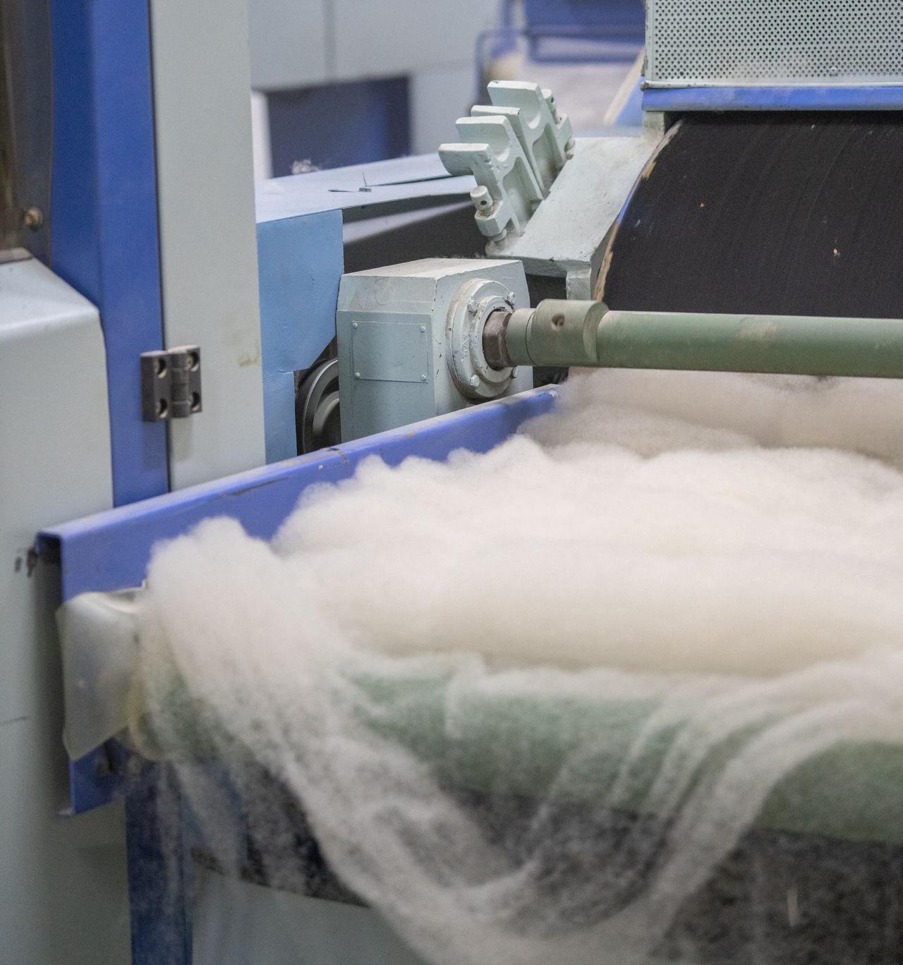 In einer Produktionshalle wird mittels Maschinen ein Wollfvlies zur weiteren Verarbeitung produziert