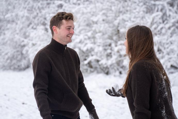 Zwei Modelle tragen dunkelbraune Strickjacke aus Yakwolle und stehen lachend in einer Schneelandschaft