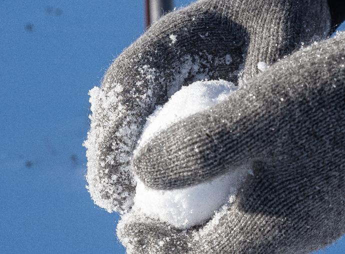 Detailfoto eines grauen Fäustlings aus Yakwolle mit Schneeball in den Händen