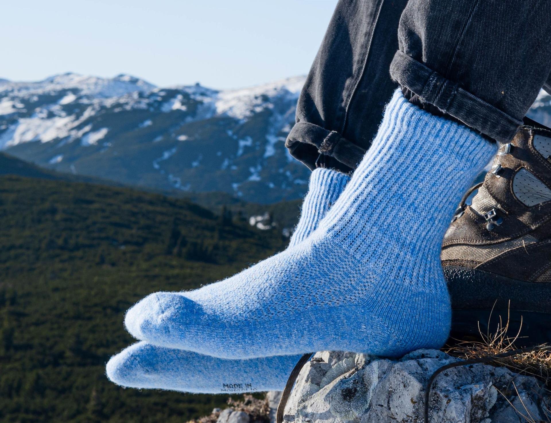 Modell trägt himmelblaue Socken aus Schafwolle undim Hintergrund ist eine Berglandschaft zu sehen.
