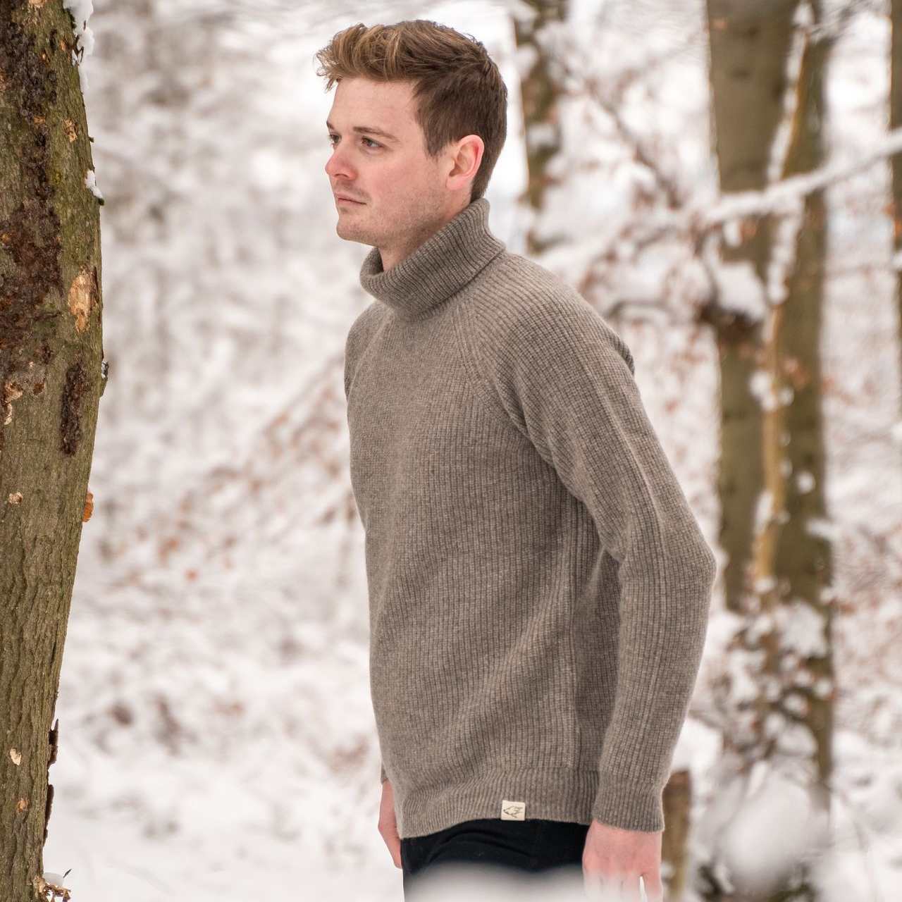 Ein Mann trägt einen grauen Rollkragenpullover und läuft durch Schnee im Wald