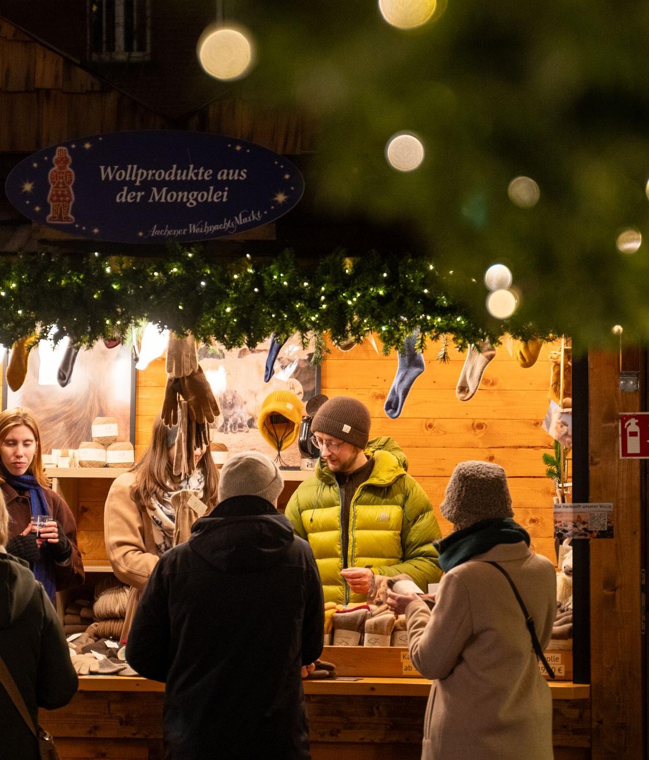 Personen stehen vvor einem Weihnahtsmarktstand mit der Aufschrift "Wollprodukte aus der Mongolei"