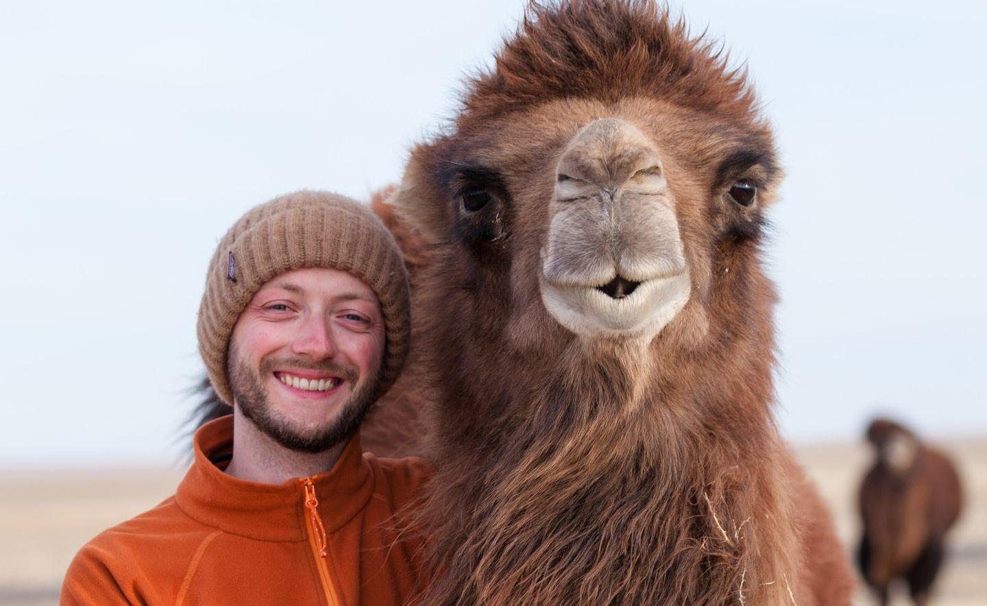 Ein Mann steht lachend neben einem Kamel