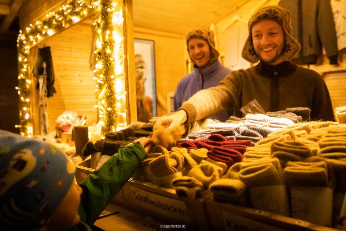 Ein warm beleuchteter Weihnachtsmarktstand mit Wollsocken an dem ein Kind an Wolle fühlt