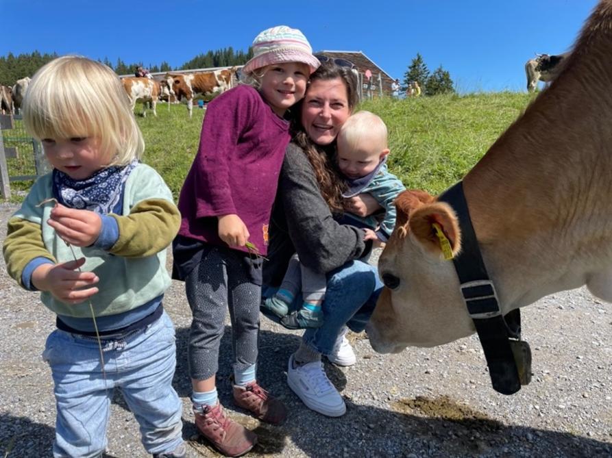 Eine junge Frau mit drei Kindern neben einer schnuppernden Kuh