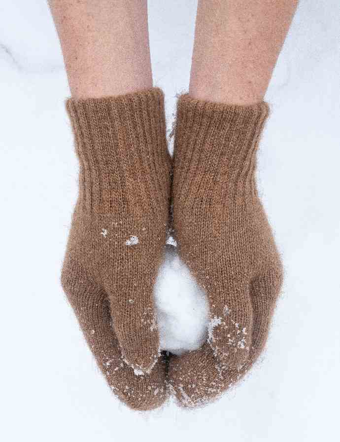 Ein Schneeball wird von braunen Handschuhen gehalten