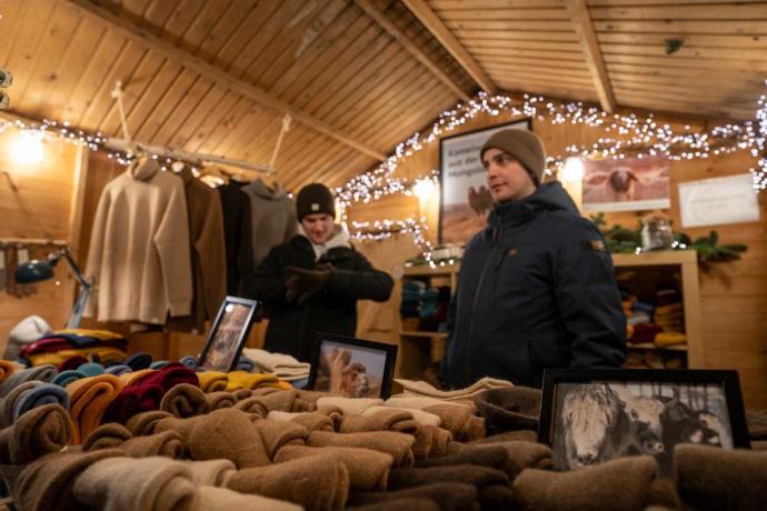 Ein Weihnachtsmarktstand mit verschiedenen Wollprodukten, liebevoll dekoriert mit Lichterketten.