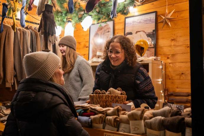 Besucher in Winterkleidung, die sich an einem gut besuchten Weihnachtsmarktstand umsehen.