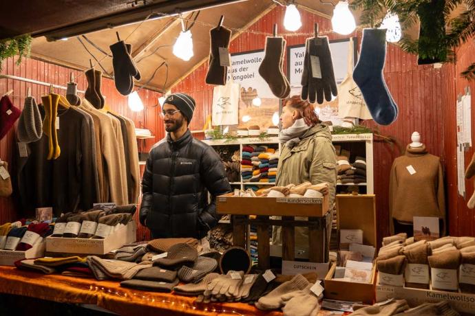 Zwei Personen hinter einem weihnachtlich dekorierten Stand mit Socken, Handschuhen und Wollprodukten.