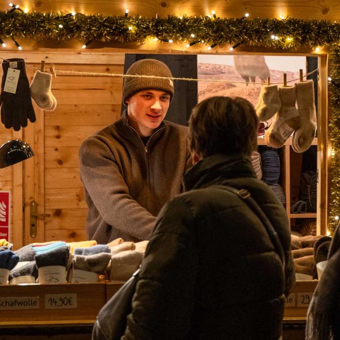 Ein Verkäufer mit Mütze, der einem Kunden an einem Weihnachtsmarktstand hilft.