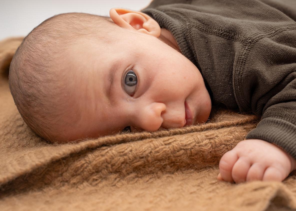 Ein Baby liegt auf einer braunen Wolldecke für Babys und schaut wach in die Kamera