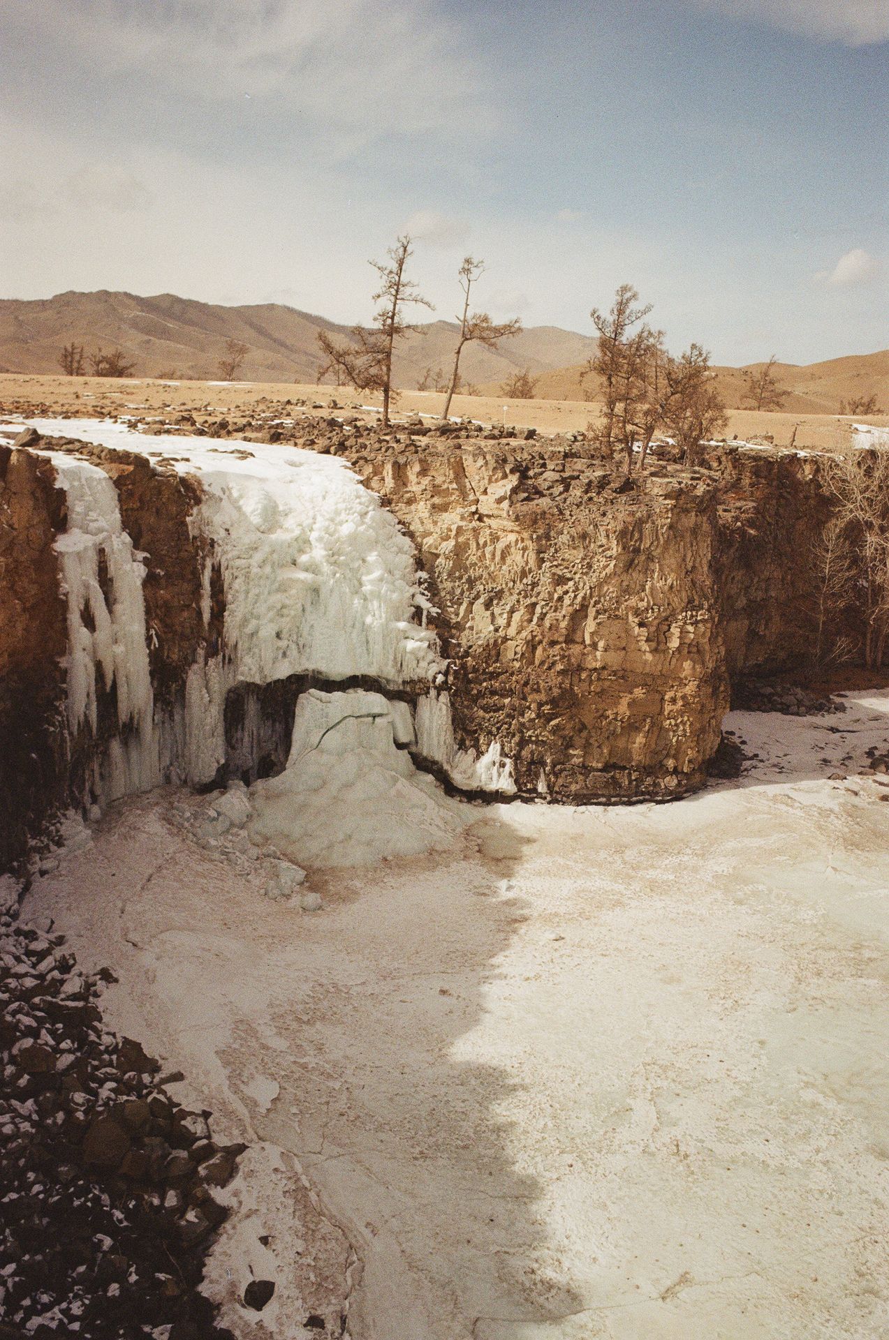Ein halb zugefrorener Wasserfall in einer trockenen Canyon-Landschaft.