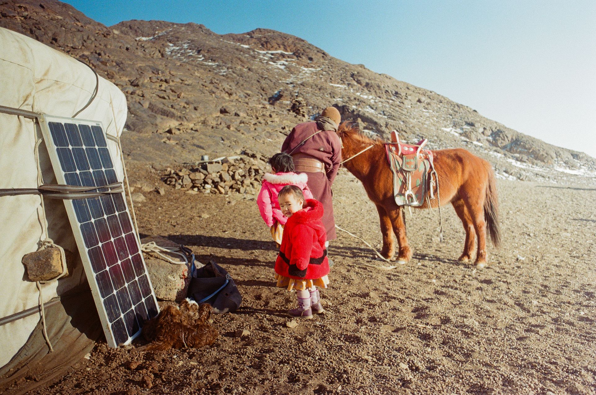 Zwei Kinder in traditioneller Kleidung neben einer Jurte mit Solarpanel und Pferd.