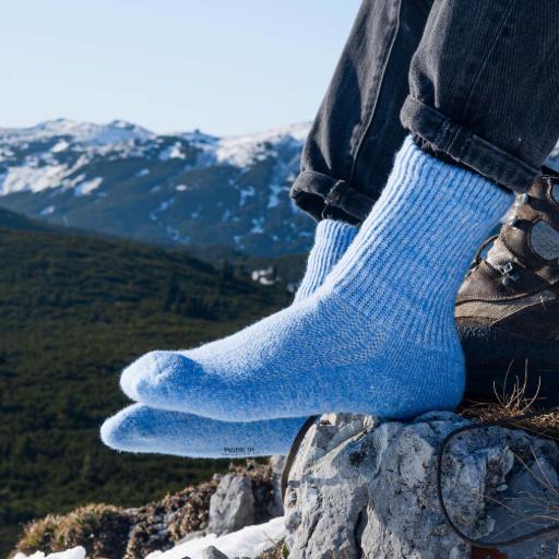Eisblaue Wollsocken werden vor einem Bergpanorama getragen an Füßen auf einem Stein