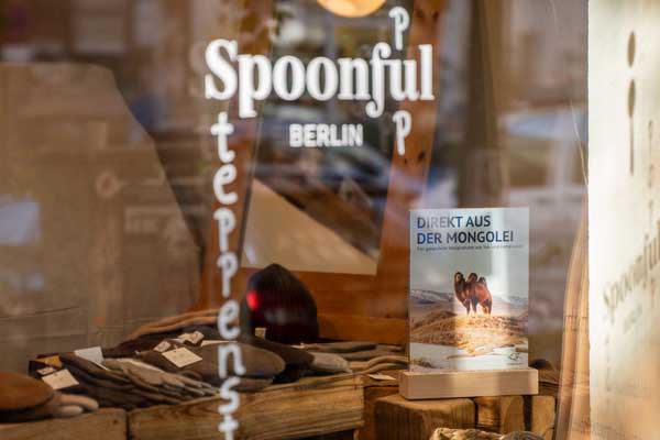 View through a bright shop window displaying the words "SPOONFUL BERLIN" into a store where knitted hats and accessories are on display.
