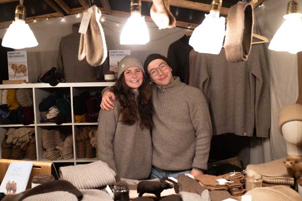 Two people wearing natural wool products laugh at the camera behind a stand.
