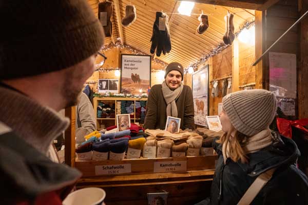 Two people are standing in front of a Steppenstrolch Christmas market stall.