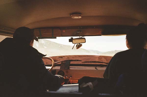 Den Blick gerade aus, auf das nächste Steinloch gerichtet. Siluetten von zwei Personen in einem Kleinbus als Fahrer und Beifahrer