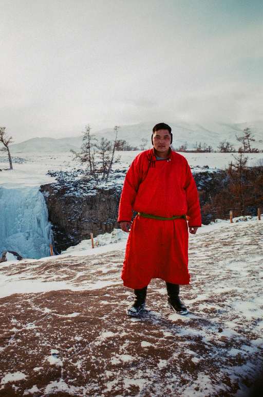 Ein Mann in roter traditioneller Kleidung der Mongolei steht vor einem gefrorenen Wasserfall