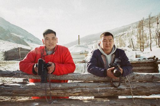 Zwei mongolische Männer stehen an einem Zaun und schauen in die Kamera