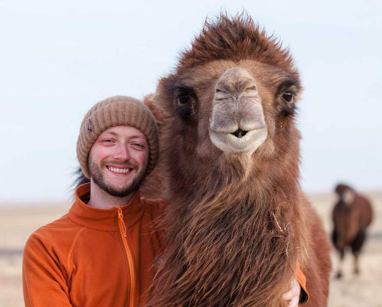 Junger Mann mit Wollmütze neben einem Kamel