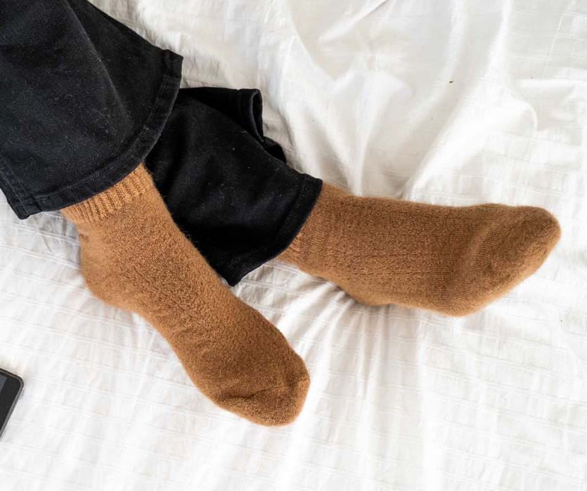 Füße in braunen Socken überschlagen auf einem weißen Bett