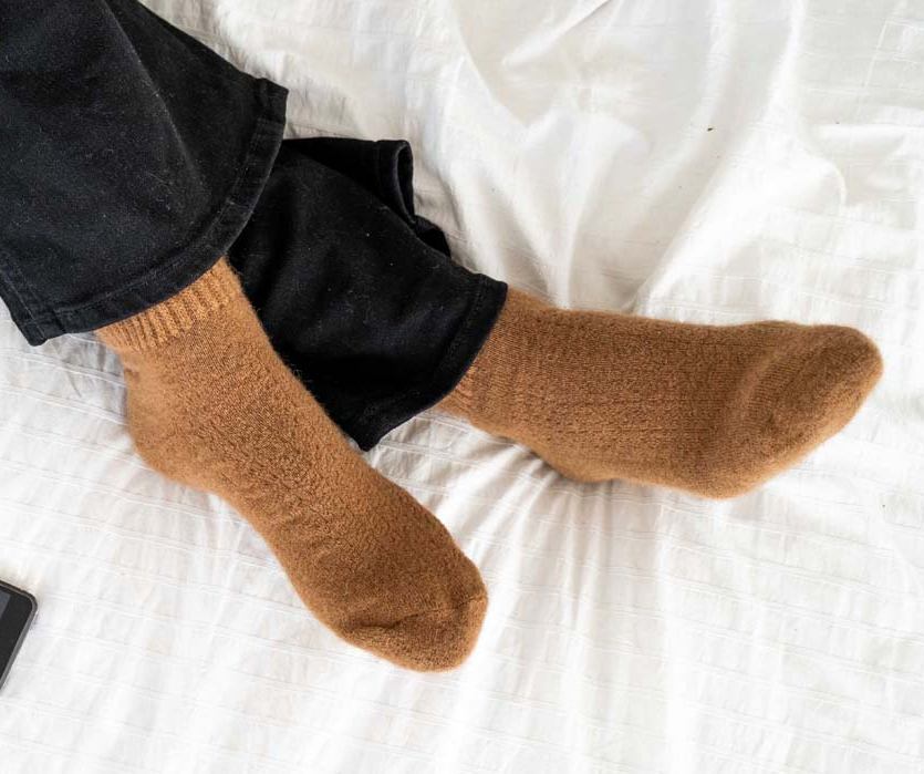 Feet in brown socks roll over on a white bed