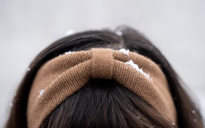 Braunes Stirnband mit etwas Schnee zwischen schwarzen Haaren