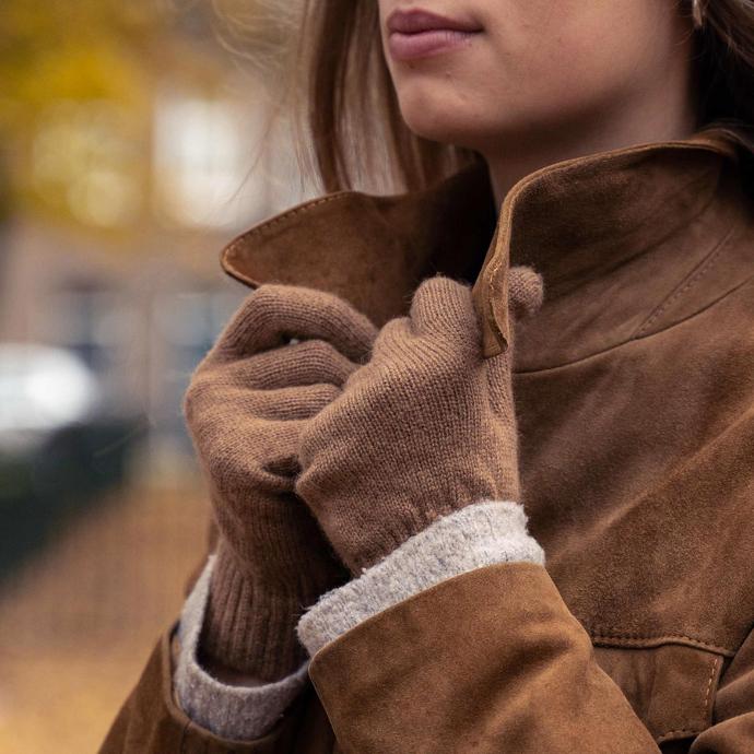 Brown woollen gloves hold the collar of a brown jacket