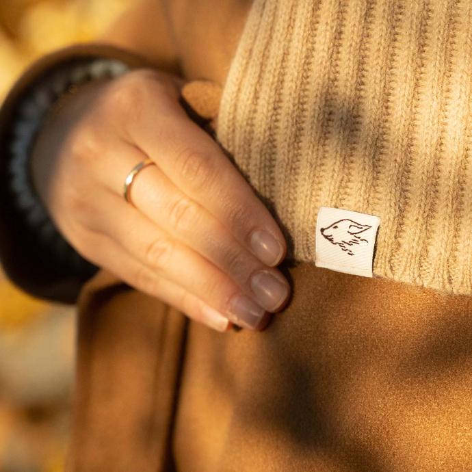 Fingers holding a woollen scarf with a small steppenstrolch logo on it
