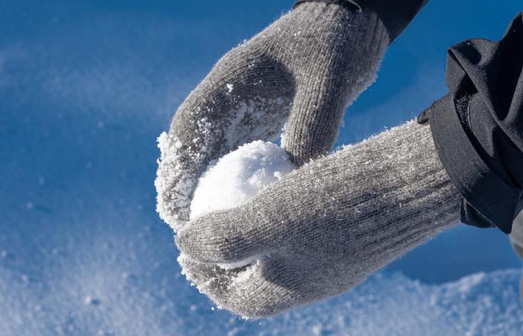 Graue Fäustlinge halten Schneeball