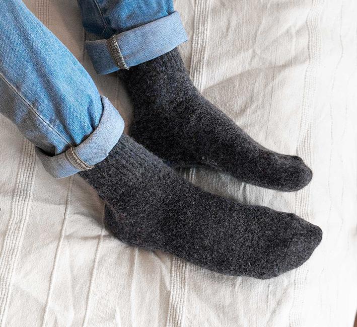Wollsocken in steingrau werden auf einem weißen Bettdeck getragen